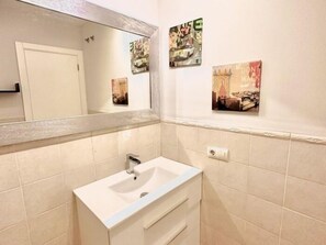 A bathroom with a white sink, mirror, and tiled walls. There are three framed pictures on the wall. - Apartment with large terrace in Costa Adeje. (Costa Adeje)
