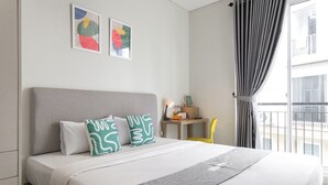 A neatly made bed with a grey headboard, two pillows with a green and white abstract pattern, and a grey throw blanket. There are two framed abstract paintings on the wall above the bed. - Mono Coliving at BSD City (Pagedangan)