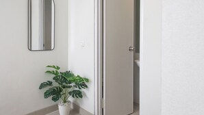 A hallway with a potted plant, a mirror, and a door leading to a bathroom. - Mono Coliving at BSD City (Pagedangan)