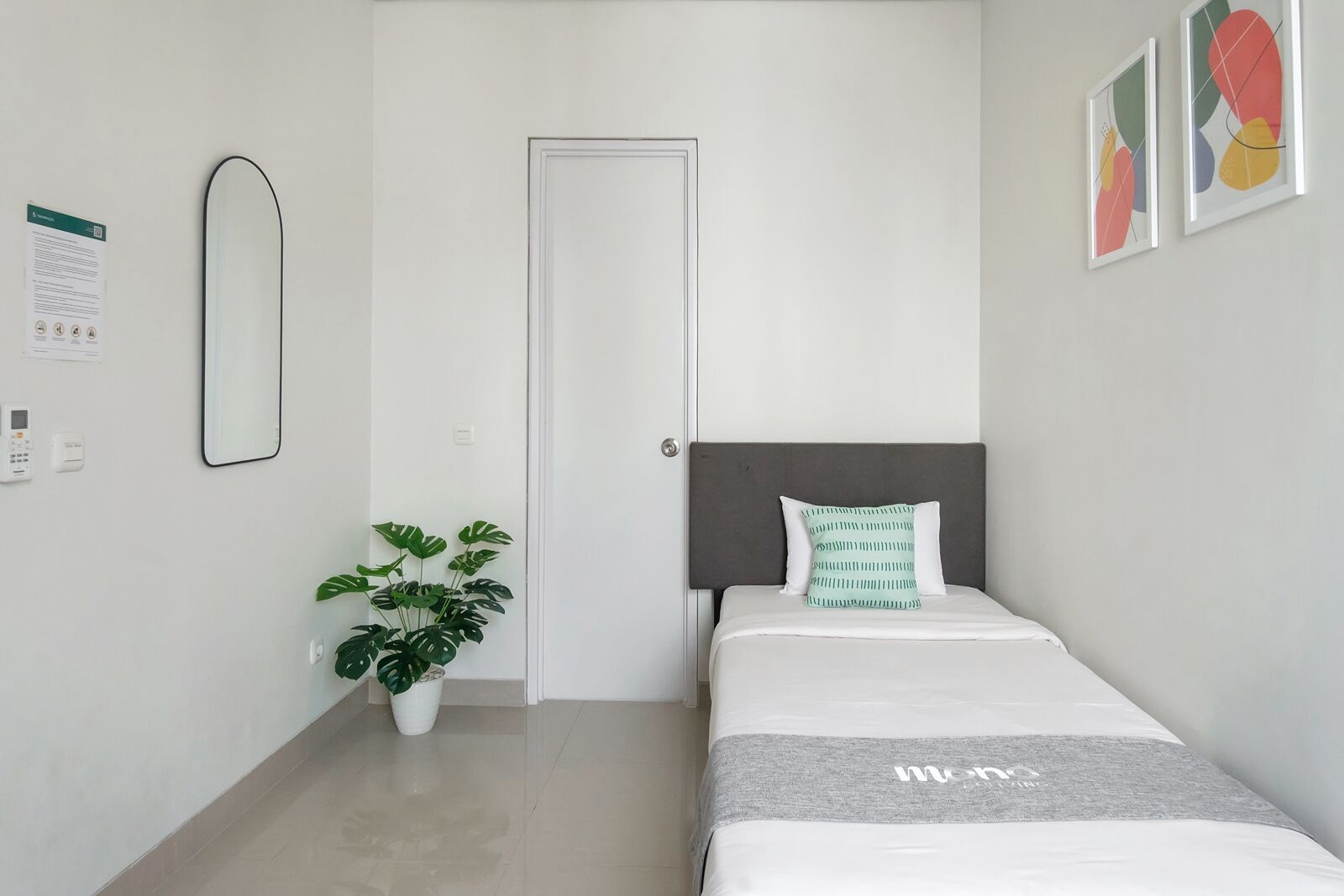 A bedroom with a bed, a potted plant, a door, and a wall-mounted mirror.