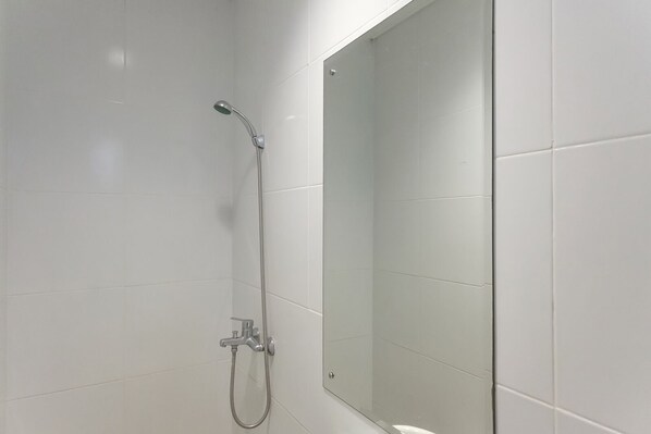 A modern bathroom with white tiles, a glass shower enclosure, and a visible showerhead and faucet. - Mono Coliving at BSD City (Pagedangan)