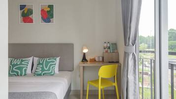 A hotel room with a bed, a desk with a chair, a lamp, and two abstract paintings on the wall.