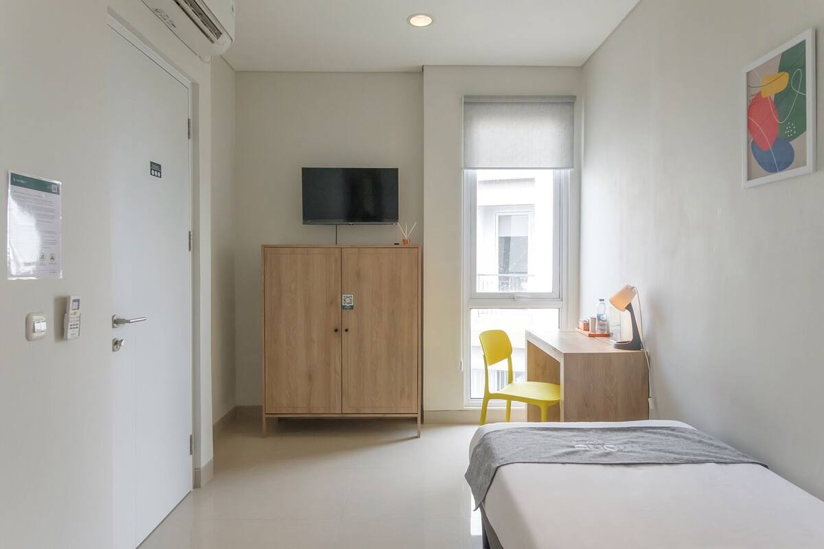 A bedroom with a bed, a desk, a chair, a TV, and a wardrobe.