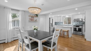 A modern kitchen with white cabinetry, a central island with stools, and a chandelier. - Stunning Cape Home Near Chatham (Brewster)