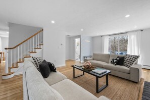 Un salon moderne avec un escalier, un ensemble de canapés, une table basse et une vue dégagée sur l’extérieur grâce à une grande fenêtre.