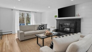 A modern living room with a fireplace, a sofa, a coffee table, and a television. - Stunning Cape Home Near Chatham (Brewster)