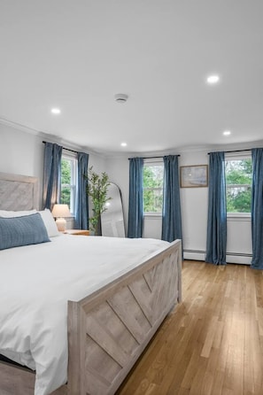 Ein Schlafzimmer mit Bett, Nachttisch, Lampe, Pflanze und einem Fenster mit Vorh ängen.