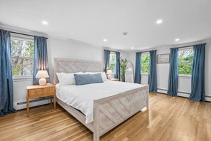 Un dormitorio con cama, mesitas de noche y ventana con cortinas.