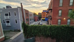 Une rue résidentielle bordée d’immeubles, avec une voiture garée et une haie.
