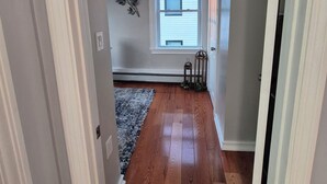 Un couloir doté d’un plancher en bois, d’une fenêtre avec des stores, d’un élément décoratif mural et d’une porte située à droite.