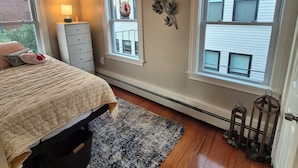 Une chambre à coucher avec un lit, une commode, deux fenêtres et un radiateur.