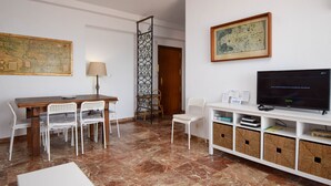A room with a wooden dining table, white chairs, a TV on a white stand, a map on the wall, and a door with a decorative screen. - Ref: 326 Beach front apartment on the promenade with beautiful sea view (Fuengirola)