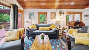 Ein gemütliches Wohnzimmer mit Holzboden, einem grauen Sofa mit gelben Kissen, einem Couchtisch mit Blumen und einem farbenfrohen Teppich.