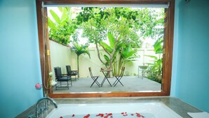 Une salle de bain avec une baignoire remplie de pétales de roses, un lavabo et une vue sur une terrasse extérieure avec des chaises et une table.