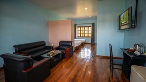 Habitación de hotel con sofá, una pequeña mesa con libros, cama, televisión y ventana con cortinas.