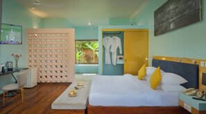 A hotel room with a bed, bedside table, and a desk with a chair. There is a window with a view of greenery outside.