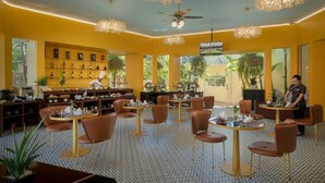 Un restaurante con varias mesas y sillas, un cocinero al mostrador y una zona de bar con estantes llenos de botellas.