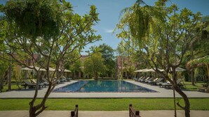 Une piscine entourée de chaises longues et d’arbres, sous un ciel dégagé.