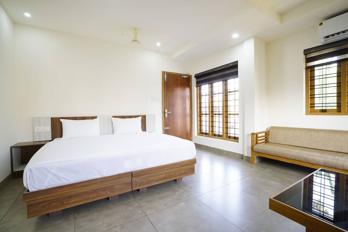 Quarto de hotel moderno com uma cama grande, um sofá, uma mesa pequena e uma janela com persianas.