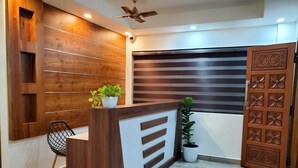 A reception area with a wooden reception desk, a black chair, and a potted plant. - Halo Residency (Kanayannur)