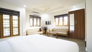 A hotel room with a large bed, a sofa, a desk with a chair, a television, and a wardrobe. - Halo Residency (Kanayannur)
