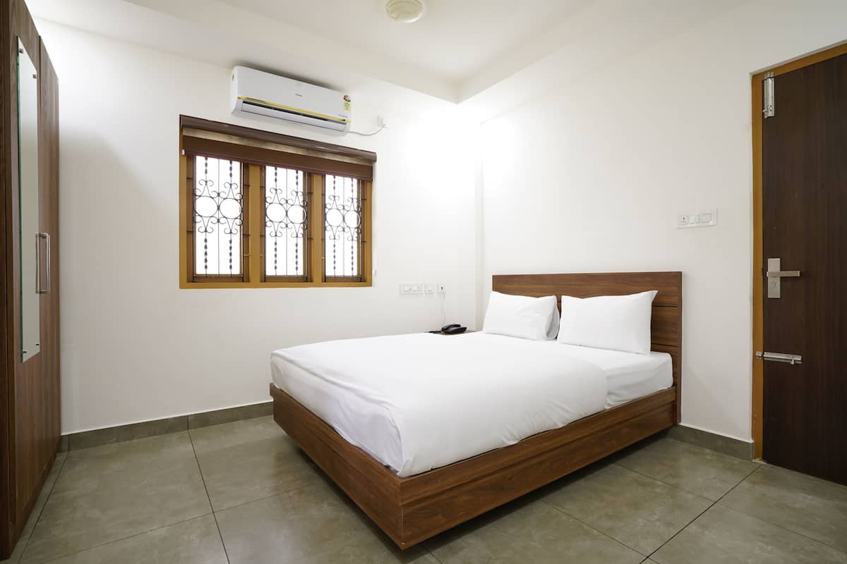 Quarto com cama de madeira, roupa de cama branca, janela com grades decorativas e ar condicionado na parede.