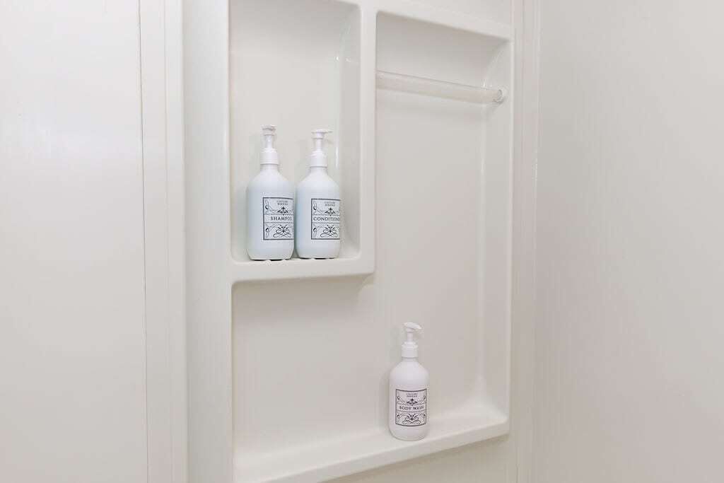 Une salle de bain avec trois flacons blancs sur une étagère, dont l’un contient un produit pour la douche.