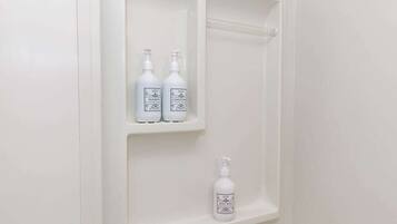 Une salle de bain avec trois flacons blancs sur une étagère, dont l’un contient un produit pour la douche.