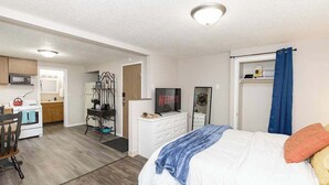 A compact bedroom with a bed, a desk, and a kitchenette. - Cozy Studio Near NDSU and Fargodome (Fargo)