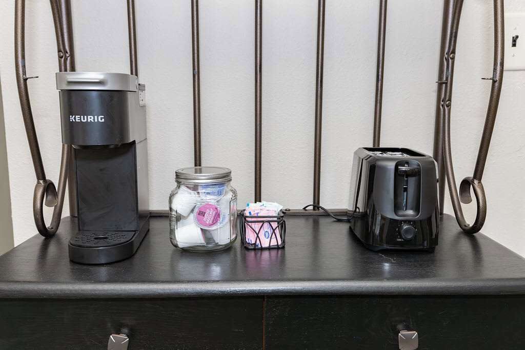 Een koffiezetapparaat, een glazen pot met een roze deksel en een broodrooster op een donker aanrecht.