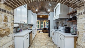 Une cuisine étroite avec des meubles blancs, un sol à motifs et des murs en briques apparentes.