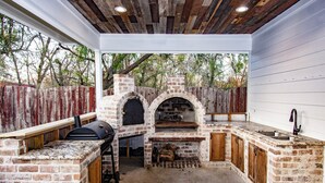 Une cuisine extérieure dotée d’un four en briques, d’un barbecue et d’un plan de travail en bois.