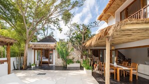 A spacious outdoor area with a dining table and chairs, a thatched-roof structure, and a stone wall. - Peaceful 3BR Villa Located in Pecatu - 10 Min to the Beach (Pecatu)