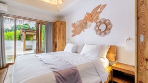 A spacious bedroom with a large bed, wooden headboard, and a view of lush greenery through large windows. - Peaceful 3BR Villa Located in Pecatu - 10 Min to the Beach (Pecatu)