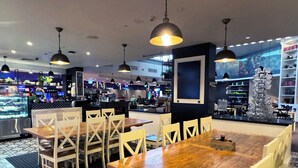 Um restaurante com mesas e cadeiras de madeira, luminárias pendentes e um balcão com uma máquina de café.