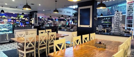 A restaurant with wooden tables and chairs, hanging pendant lights, and a counter area with a coffee machine.