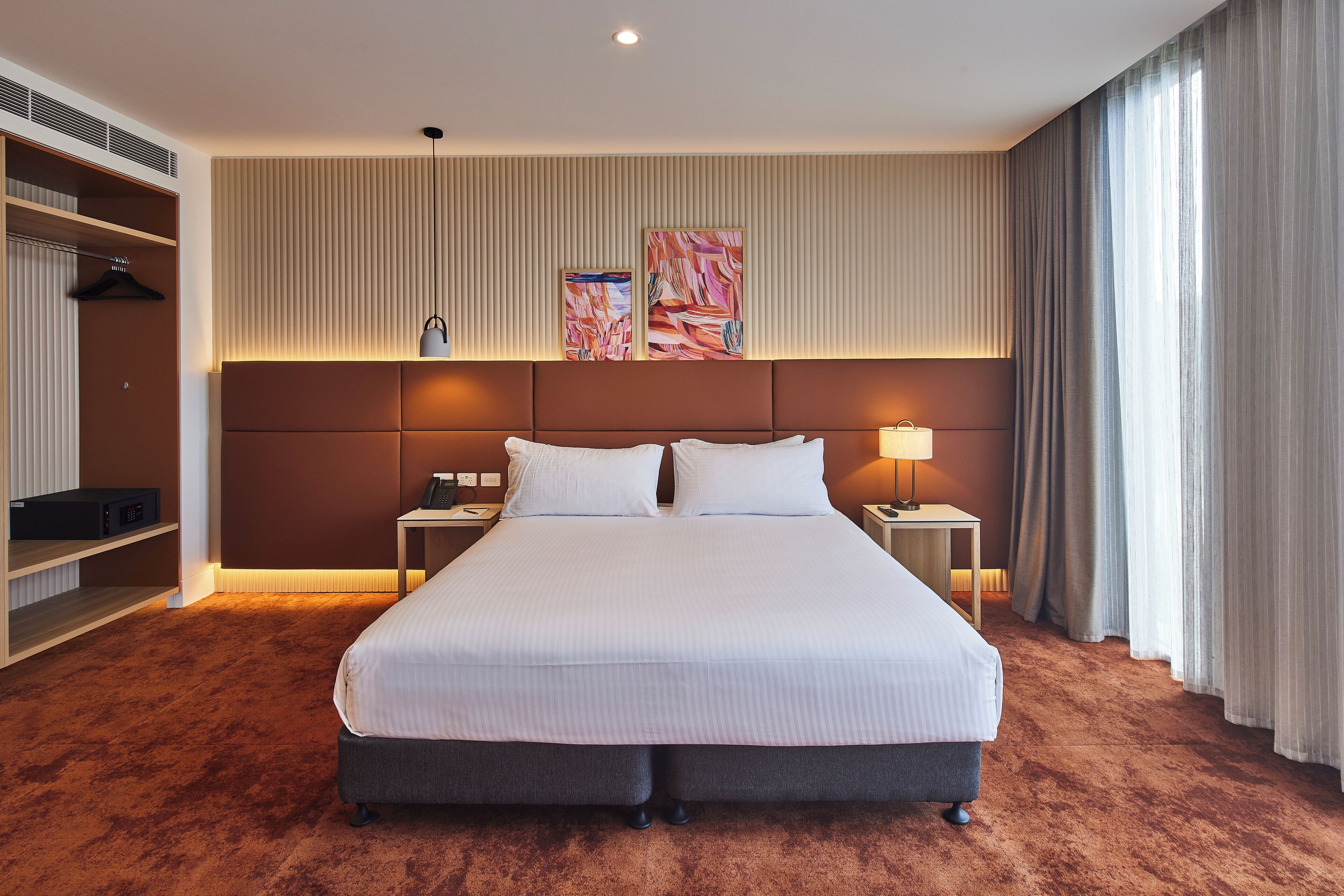 Habitación de hotel con una cama grande, dos mesitas de noche, un armario y un cabecero decorado con obras de arte.