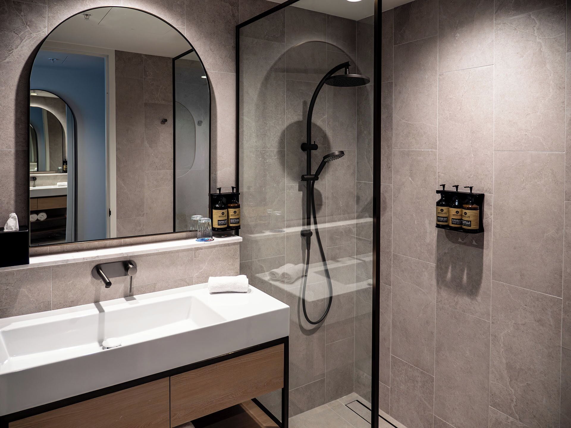 A modern bathroom with a white sink, a large mirror, and a glass-enclosed shower area.