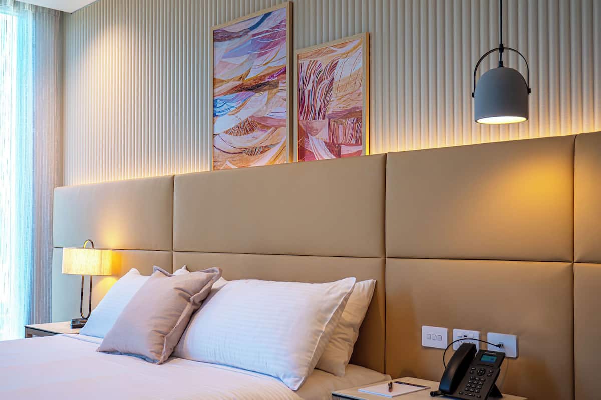 A hotel room with a large bed, a bedside table with a lamp, a phone, and two abstract paintings on the wall.