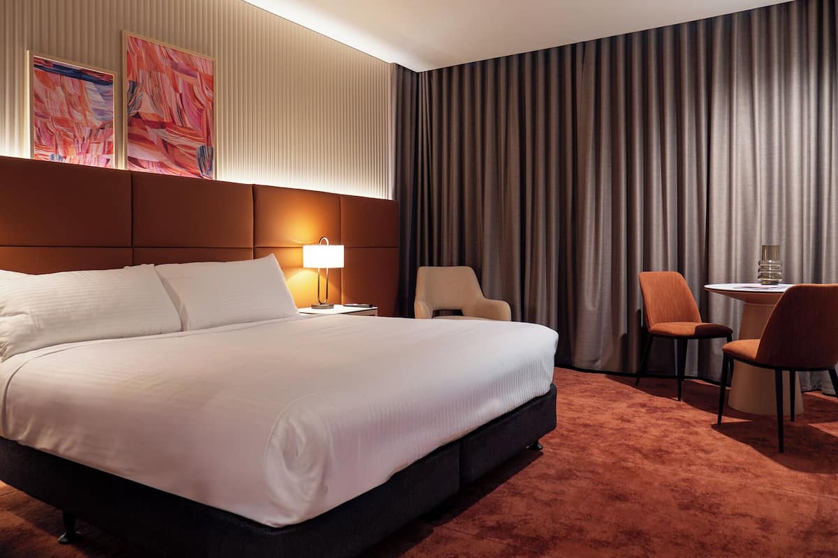 A hotel room with a large bed, two chairs, a small table, and a lamp.