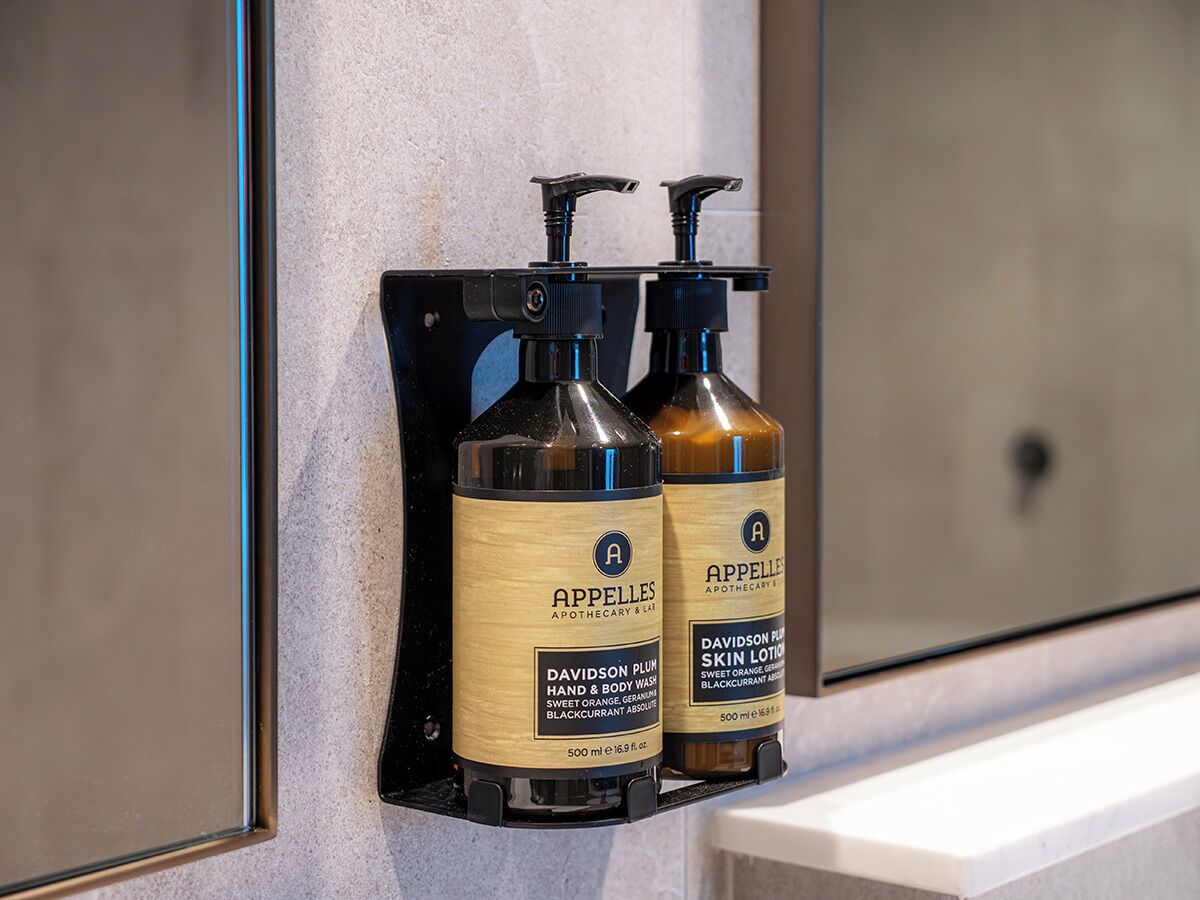 Twee flessen Davidson Plum hand- en lichaamszeep en Davidson Plum bodylotion op een zwarte zeephouder aan de muur.