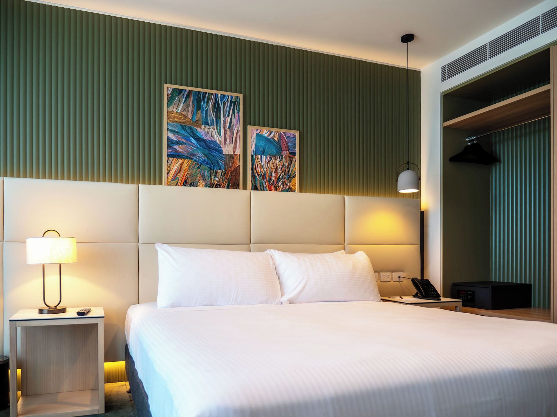 A hotel room with a large bed, a bedside lamp, a telephone, and two abstract paintings on the wall.