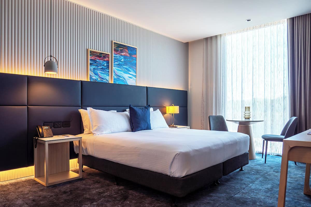 A modern hotel room with a large bed, bedside tables, a desk, and a chair.
