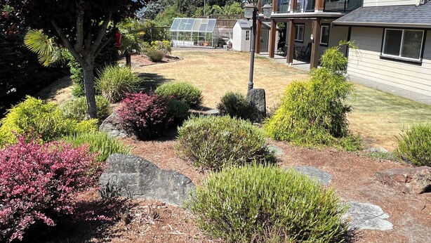 A residential area with a well-maintained lawn, a greenhouse, and a two-story house with a balcony.