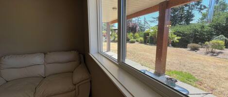 Una habitación con un sofá color beige frente a una pared, un ventanal con vistas a un jardín y zona de estar exterior.