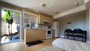 A compact kitchen with a refrigerator, oven, and sink. There is a small dining area with two chairs and a sofa.