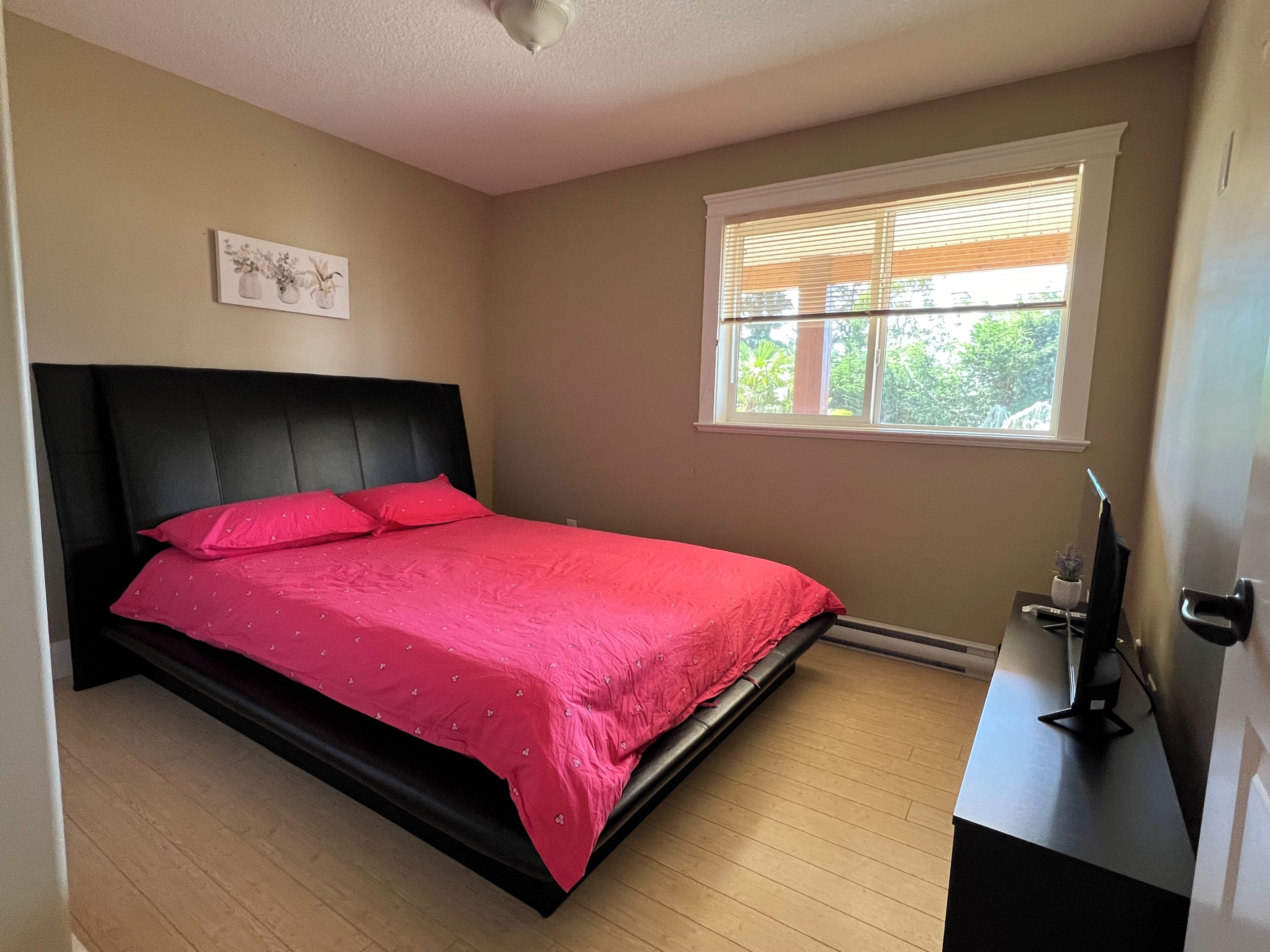 Une chambre à coucher avec un lit, une fenêtre avec des stores, un ventilateur de plafond et une petite table sur laquelle est posée une plante.
