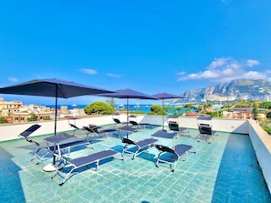 A rooftop pool with sun loungers and umbrellas, overlooking a coastal town and a mountain. - Mongibello rooftop (Palermo)