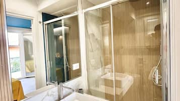 Un baño moderno con ducha de vidrio, un lavamanos blanco y un espejo grande.