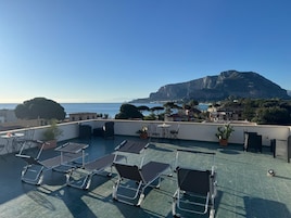 Terraço no telhado com cadeiras de descanso, mesa e plantas em vasos.